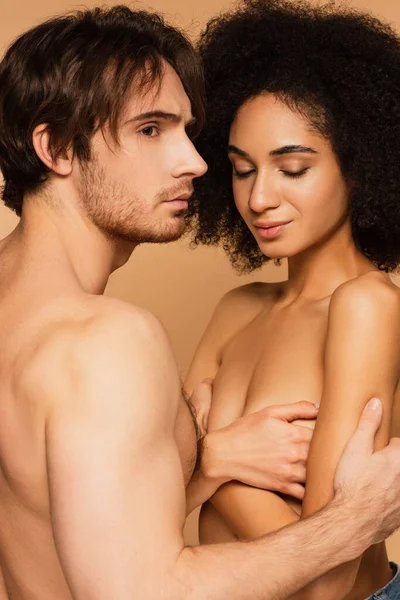 Topless hispanic woman covering breast with crossed arms near sexy man isolated on beige — Stock Photo