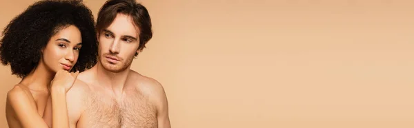 Giovane e sensuale donna latina che abbraccia spalla di uomo sexy mentre guarda la fotocamera isolata sul beige, banner — Foto stock