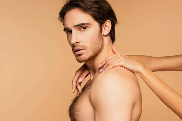 Sexy hombre sin camisa mirando a la cámara mientras mujer abrazando su cuello aislado en beige - foto de stock