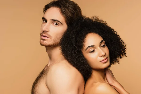 Shirtless man looking at camera while standing back to back with sexy latin woman isolated on beige — Stock Photo