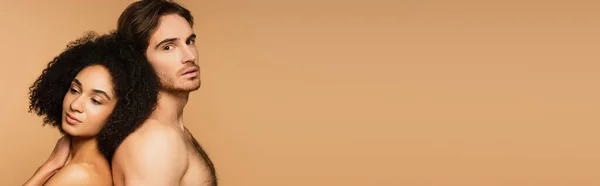Sexy homme torse nu regardant caméra tout en se tenant dos à dos à jeune femme hispanique isolé sur beige, bannière — Photo de stock