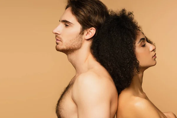 Vista laterale di uomo senza camicia in piedi schiena contro schiena con sensuale donna ispanica isolato su beige — Foto stock