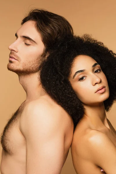 Mujer hispana seductora y hombre sin camisa con los ojos cerrados de pie espalda con espalda aislada en beige - foto de stock