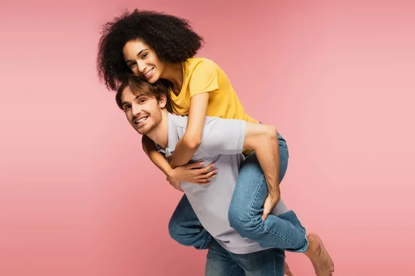 Giovane e felice coppia multietnica sorridente alla macchina fotografica mentre si diverte isolato sul rosa — Foto stock