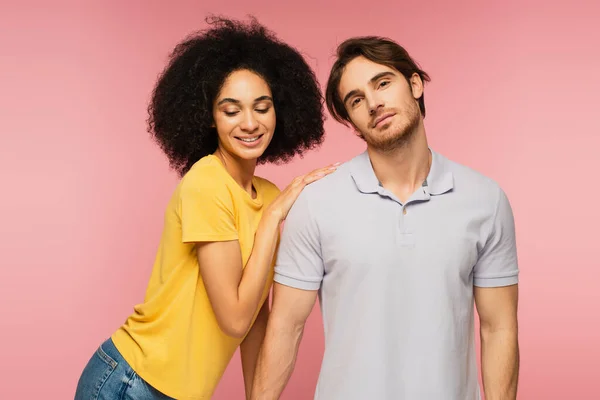 Bouclé hispanique femme appuyé sur épaule de jeune homme regardant caméra isolé sur rose — Photo de stock