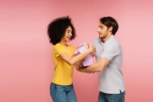 Joven hombre regalando un montón de regalos a asombrada novia latina aislado en rosa - foto de stock