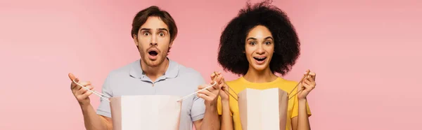 Thrilled interracial couple with shopping bags looking at camera isolated on pink, banner — Stock Photo