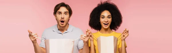 Aufgeregtes gemischtes Paar mit Einkaufstüten, die isoliert auf rosa Banner in die Kamera schauen — Stockfoto