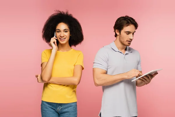 Happy latin woman calling on mobile phone near man using digital tablet isolated on pink — Stock Photo