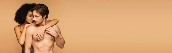 Donna ispanica riccia che abbraccia il busto muscolare dell'uomo sexy senza maglietta isolato sul beige, banner — Foto stock