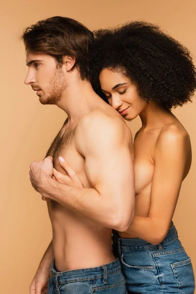 Topless hispanic woman with closed eyes hugging torso of shirtless man isolated on beige — Stock Photo