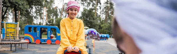 Cheerful arabian son playing on playground near blurred father, banner — Stock Photo