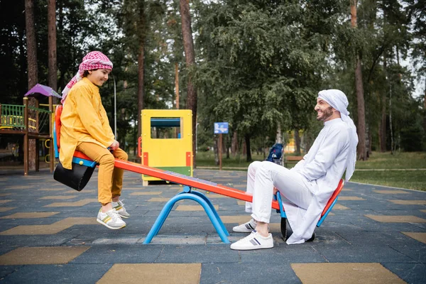 Vista laterale del figlio e del padre arabo che giocano nel parco giochi — Foto stock