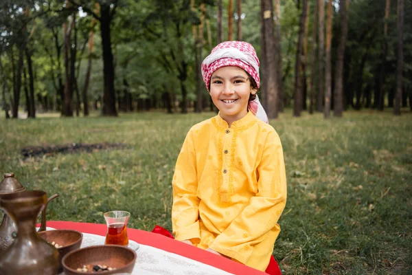 Smiling arabian boy looking at camera near tea in park — Stock Photo