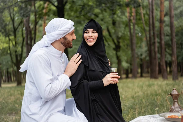Arabian man hugging wife in hijab holding tea in park — Stock Photo