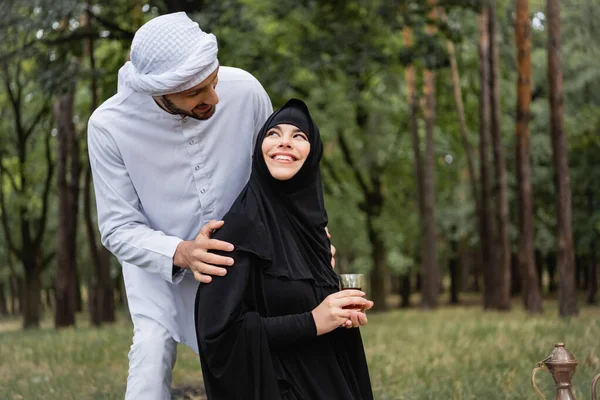 Arabian man in traditional clothes hugging wife with tea in park — Stock Photo