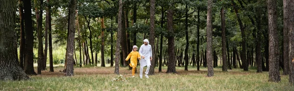 Улыбающиеся мусульмане отец и сын бегают в парке, знамя — стоковое фото