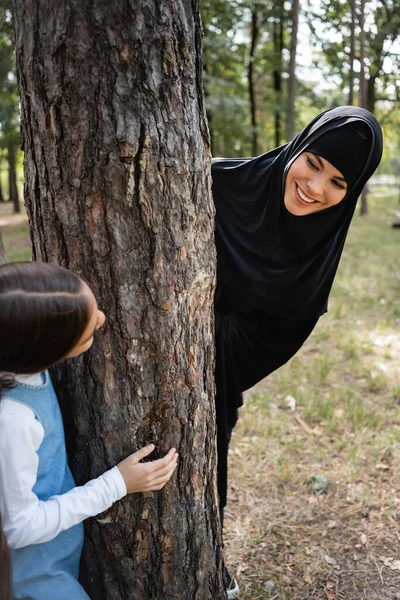 Muslim mother in hijab looking at daughter near tree in park — Stock Photo