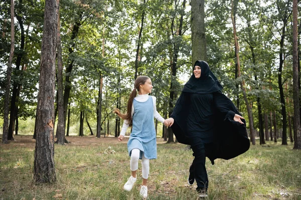 Smiling arabian woman in hijab walking near daughter in park — Stock Photo