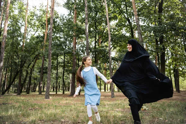 Smiling arbian mother and daughter holding hands while running in park — Stock Photo