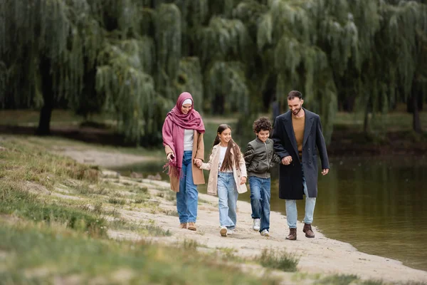 Smiling muslim kids walking near parents and lake in park — Stock Photo