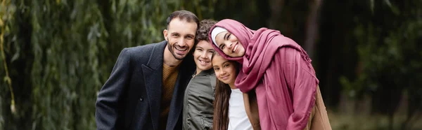 Familia árabe con niños sonriendo a la cámara en el parque, pancarta - foto de stock