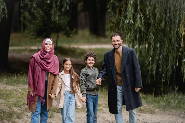 Веселые мусульманские родители, гуляющие рядом с детьми в парке осенью — стоковое фото