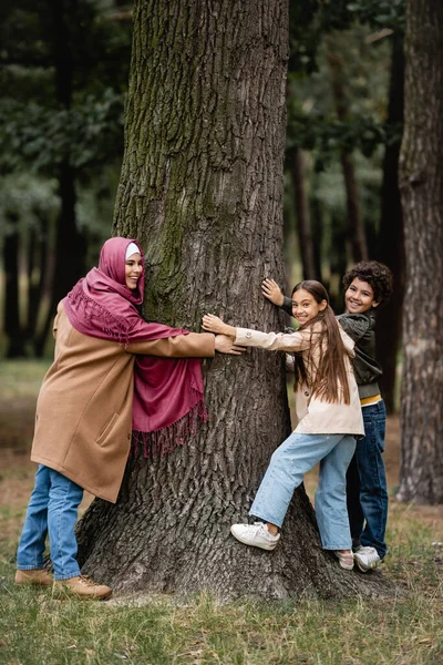 Femme musulmane joyeuse et enfants étreignant l'arbre dans le parc — Photo de stock