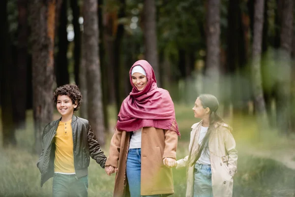 Niños felices caminando cerca de la madre árabe en el parque - foto de stock