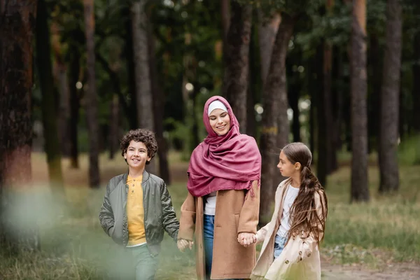 Мусульманка в хиджабе держит за руки детей в парке — стоковое фото