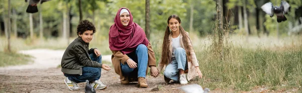 Muslim family looking at blurred birds in park, banner — Stock Photo