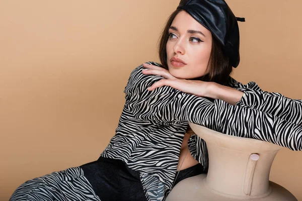 Young woman in zebra print outfit and black beret posing near clay vase isolated on beige — Stock Photo