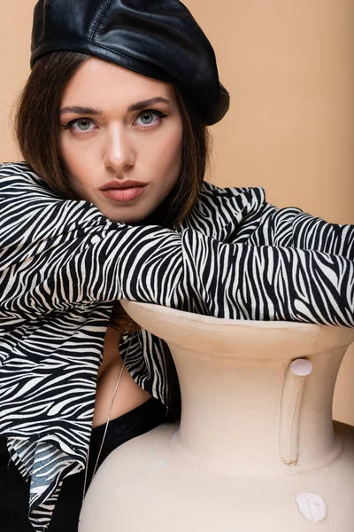 Young model in zebra print outfit and black beret posing near clay vase isolated on beige — Stock Photo