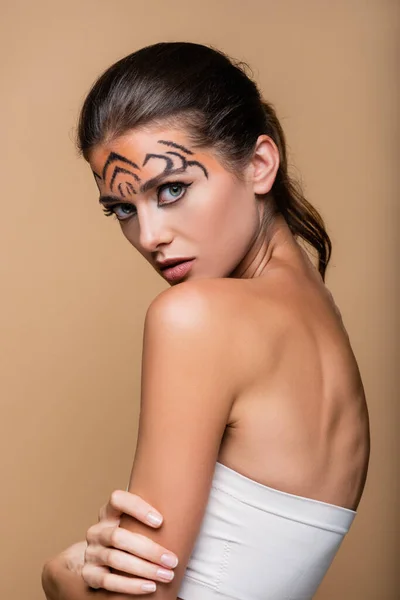 Гарна жінка з голими плечима і тигровим макіяжем позує ізольовано на бежевому — стокове фото