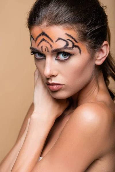 Bonita mujer con maquillaje de tigre mirando a la cámara aislada en beige - foto de stock