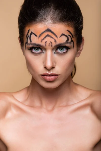 Молодая модель с макияжем тигра, смотрящая на камеру, изолированную от бежевого — стоковое фото