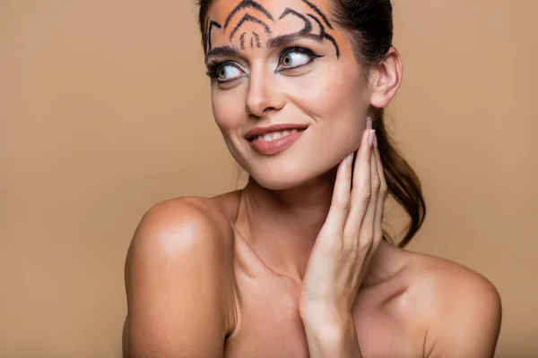 Fröhliche Frau mit nackten Schultern und Tiger-Make-up, die isoliert auf beige schaut — Stockfoto