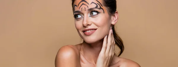 Mulher alegre com ombros nus e maquiagem tigre olhando para longe isolado em bege, banner — Fotografia de Stock