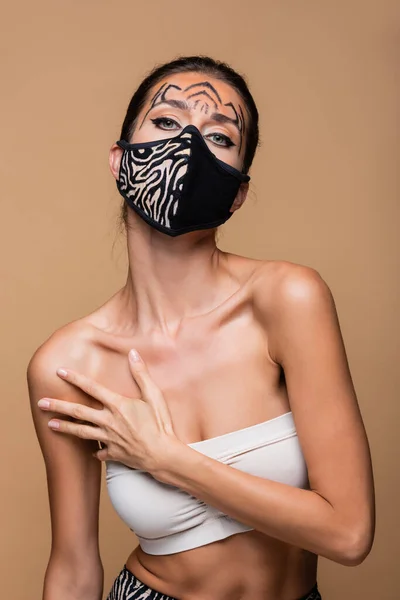 Woman with tiger makeup and animal print protective mask posing isolated on beige — Stock Photo