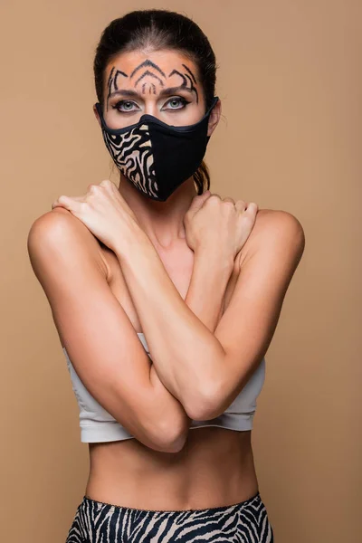 Woman with tiger makeup and protective mask posing isolated on beige — Stock Photo