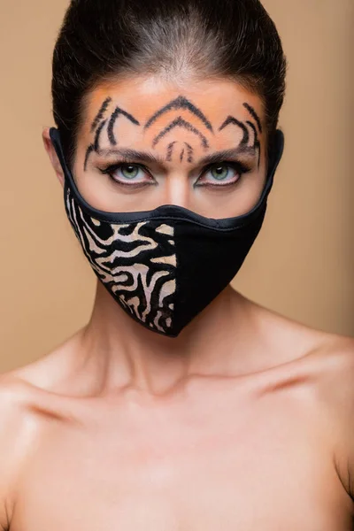 Primer plano de la mujer con el maquillaje del tigre y la máscara protectora de impresión animal posando aislado en beige - foto de stock