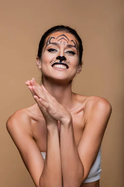 Mujer sonriente con hombros desnudos y maquillaje de tigre posando aislado en beige - foto de stock