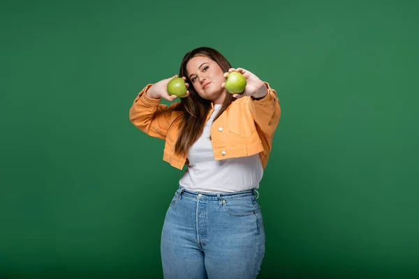 Jeune femme avec surpoids tenant des pommes et regardant la caméra isolée sur vert — Photo de stock