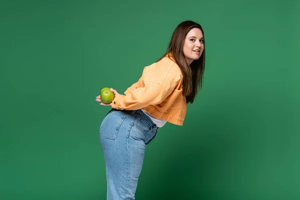 Mujer joven con sobrepeso sosteniendo manzanas aisladas en verde - foto de stock