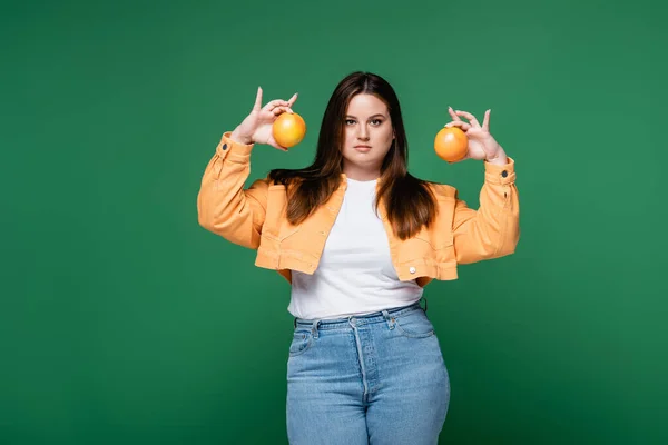 Young woman with overweight holding oranges isolated on green — Stock Photo