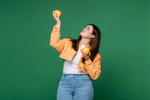 Corpo jovem mulher positiva segurando laranjas frescas isoladas em verde — Fotografia de Stock