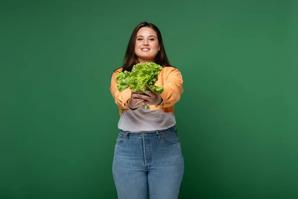 Mulher sorridente com excesso de peso segurando alface isolada em verde — Fotografia de Stock