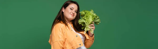 Улыбающаяся женщина с избыточным весом держит салат и глядя на камеру изолированы на зеленый, баннер — стоковое фото