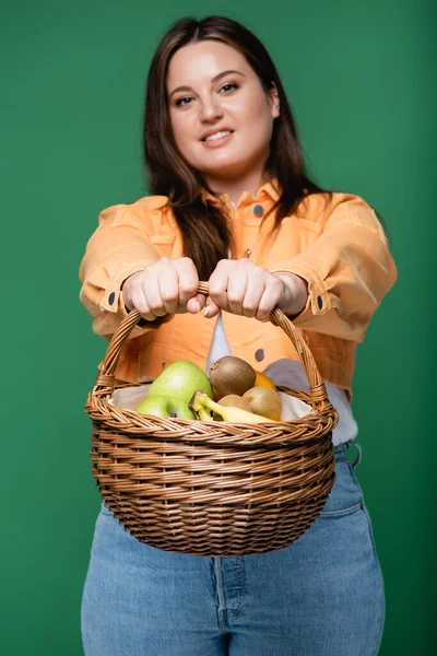 Корзина с фруктами в руках размытой женщины с избыточным весом изолированы на зеленый — стоковое фото