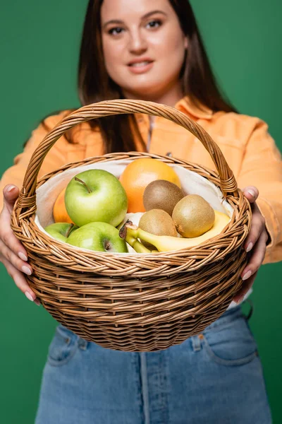 Basket with fresh fruits in hands of blurred body positive woman isolated on green — Stock Photo
